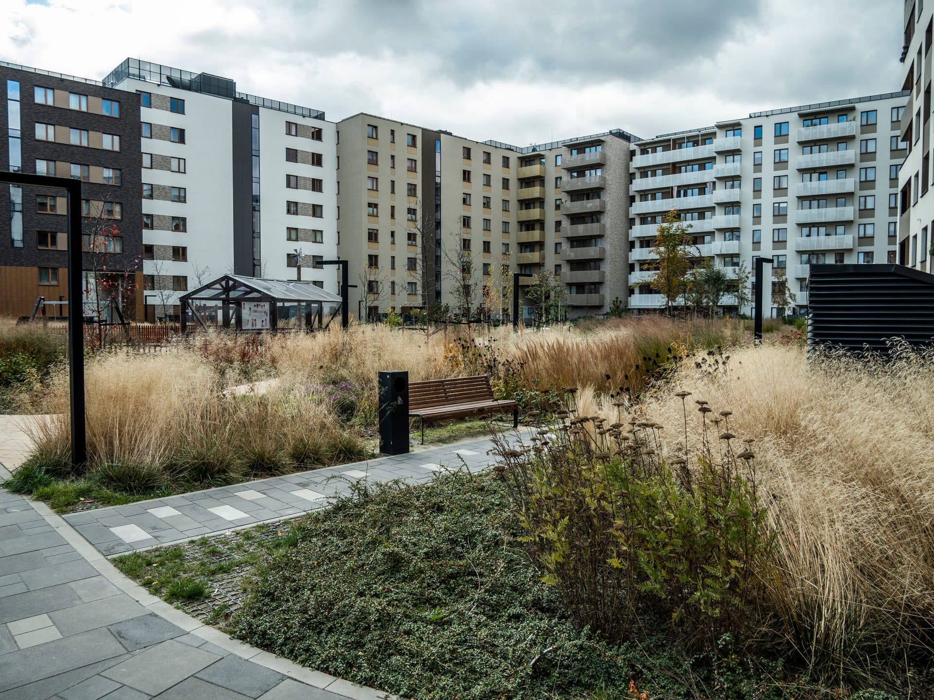 Innenhof einer Wohnanlage mit gepflasterten Wegen, Gräsern, einer Bank und mehrstöckigen Wohnhäusern.